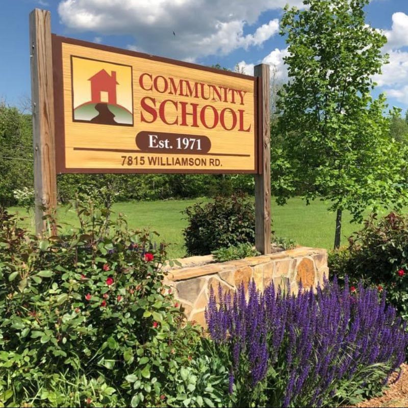 The Community School sign in Summer, surrounded by beautiful greenery.