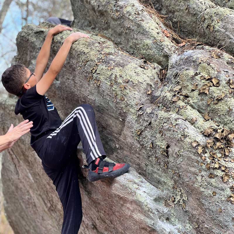 Community School has many opportunities for children to get outside—this student is rock climbing, or bouldering, with support from the teacher as needed. Shown: student rock climbing in climbing shoes.