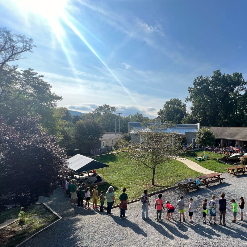 The students and teachers are forming a circle in the Community School campus during a sunny day near Roanoke, Virginia.