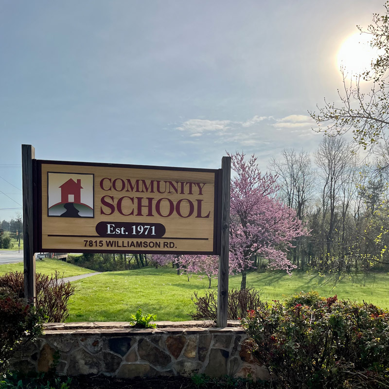 Image of Community School's sign during Spring with flowering trees in bloom in the background.