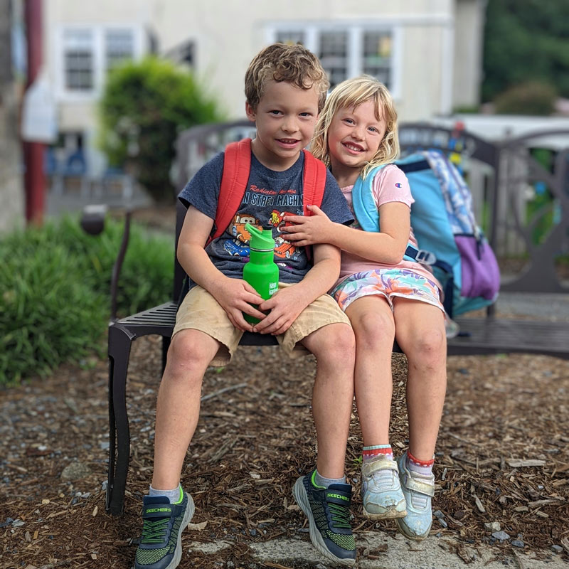 Many families choose community school after discovering that their children benefit from our smaller class sizes. Shown: Caucasian siblings embracing on the bench at the Community School campus playground.