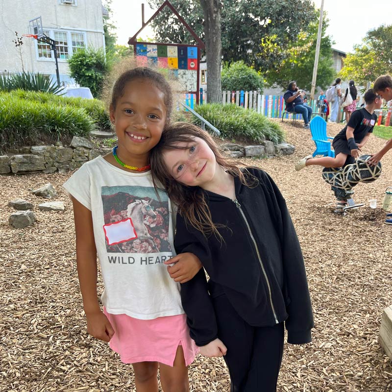 Two students, one African American and one caucasian are embracing on the Community School campus playground.