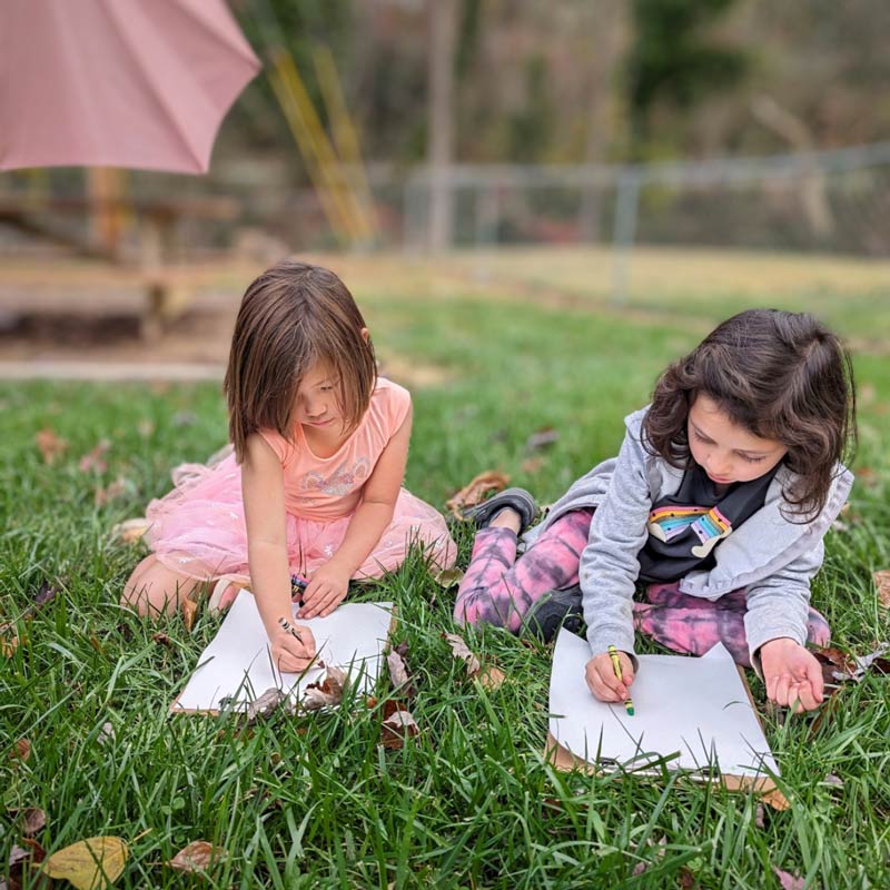 Two young caucasian girls doing their school work in the grass at Community School, a private school near Roanoke, Virginia.