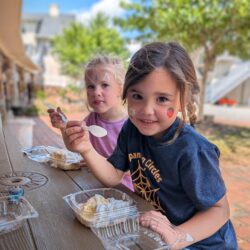 Two young girls enjoying shortcakes with smiles and their faces painted.