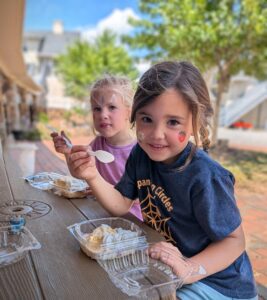 Two young girls enjoying shortcakes with smiles and their faces painted.