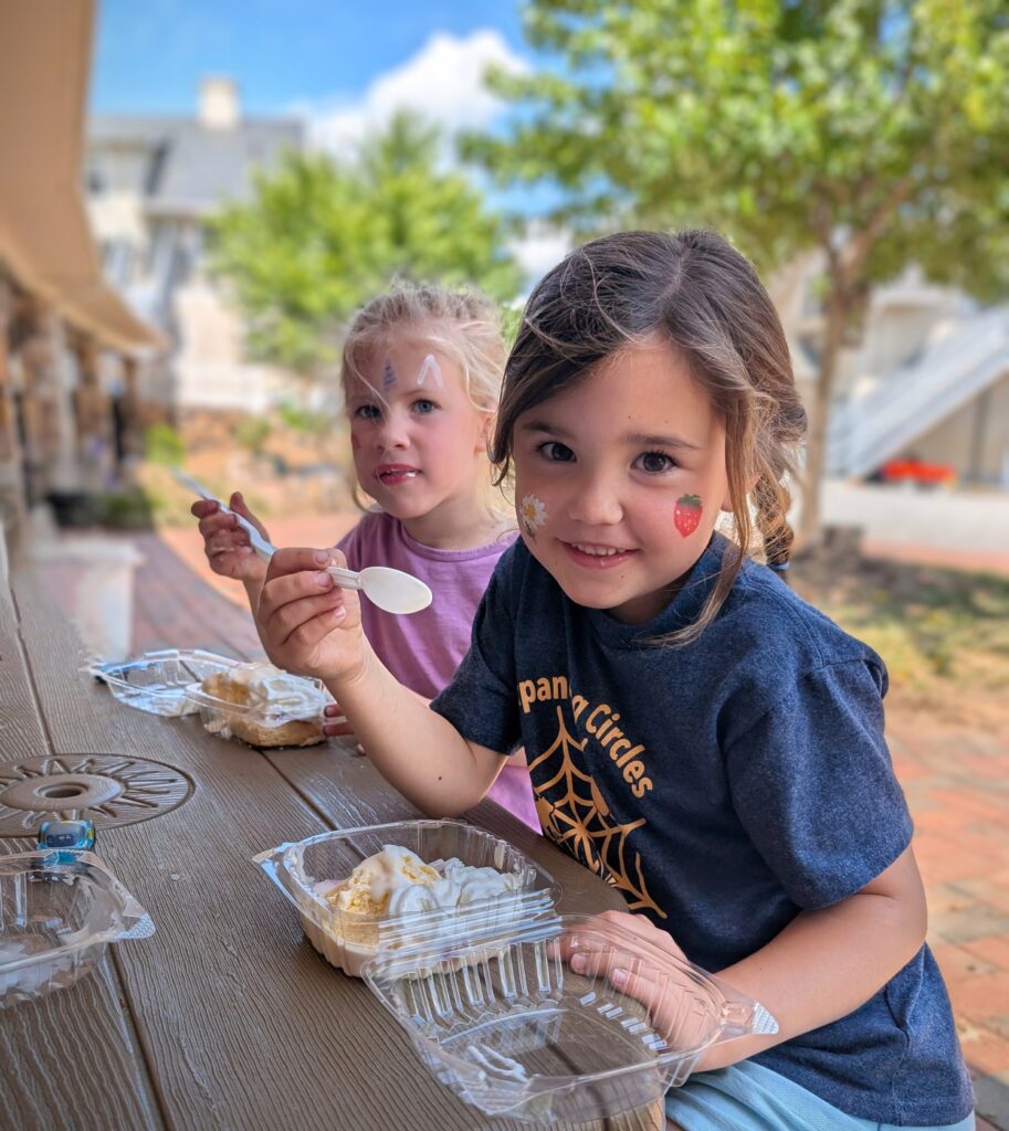 Two young girls enjoying shortcakes with smiles and their faces painted.