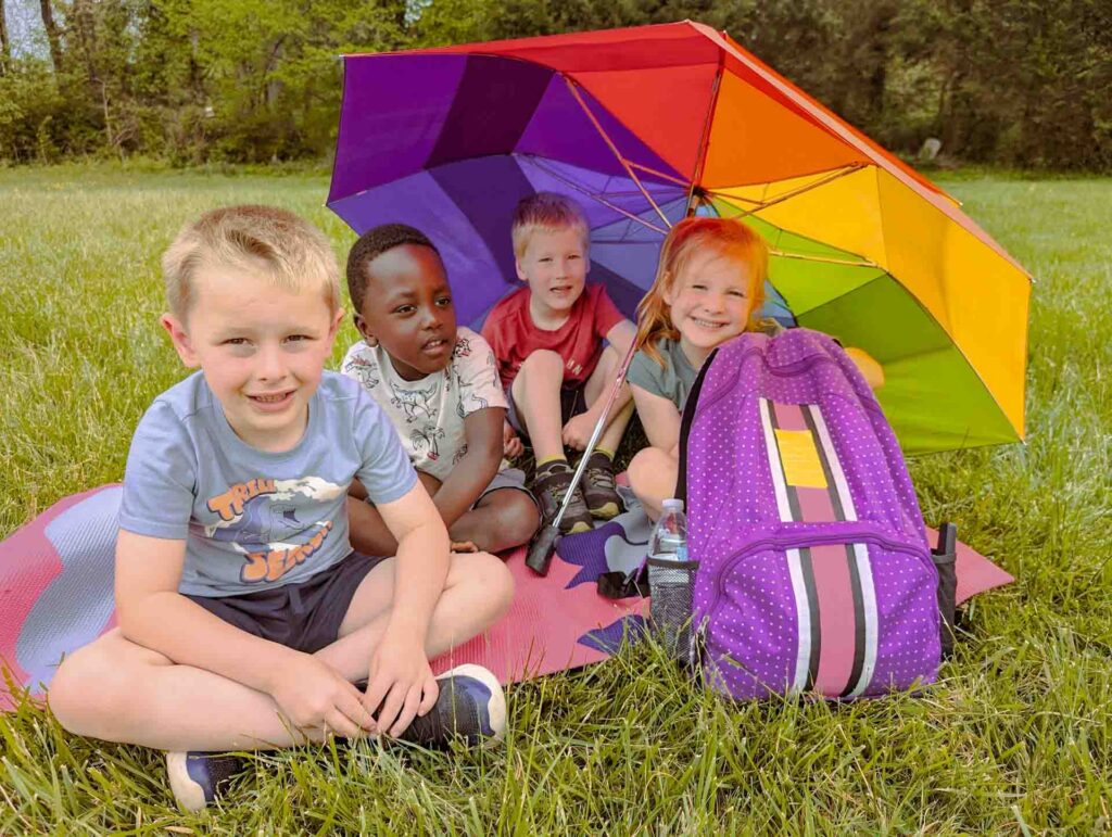 Group of smiling children with rainbow umbrella on the lawn at Community School's campus in Roanoke, Virginia.